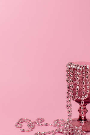 glass with a pattern on a pastel pink background. Beads hang from the edge of the cup and partially lie on the table. All objects and background are pink. Minimalism. Copy space. vertical photoの写真素材