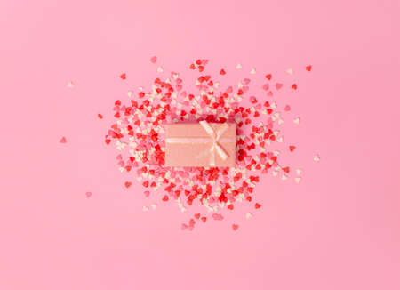pink gift box with a bow in the center of the frame on a background of scattered little sweet candy hearts on a pink background. view from above.の写真素材