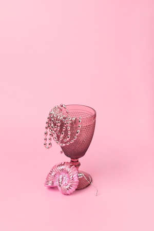 pink goblet for wine on a pastel pink background. Beads hang from the glass, and next to it is shell toy. All objects and background in pink color. Minimalism. Copy space.の写真素材