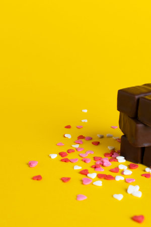 a stack of chocolates on a background of confetti from small hearts. yellow background.の写真素材