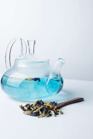 Blue herbal Butterfly pea flower tea in a glass teapot on white background. Next to the teapot are dry inflorescences. Hard shadows. Minimalismの写真素材