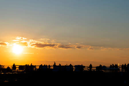 Silhouettes of young people sitting on the St. Petersburg roof against the background of the orange sunset.の写真素材