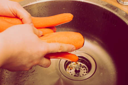 Top down view on metal sink in a modern kitchen with hands washing vegetables. old, vintage, retro style.の写真素材