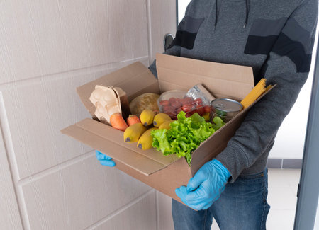A courier in blue protective gloves delivers a box of food. Home delivery conceptの写真素材