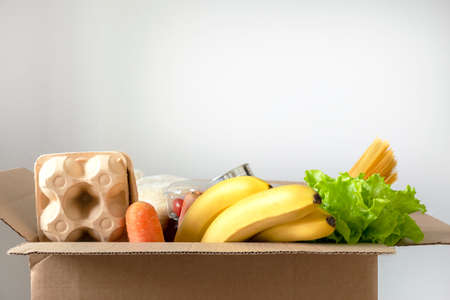Box filled with food on an isolated background. In the box are vegetables, fruits, bananas, carrots, eggs, fresh salad, spaghetti, canned foods. Concept of donation, home delivery foodの写真素材
