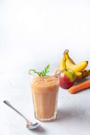 Step by step cooking smoothies. In a glass cup smoothie of apple, banana and carrot is decorated with arugula leaves. In the background are fruits and vegetables. The concept of healthy nutritionの写真素材