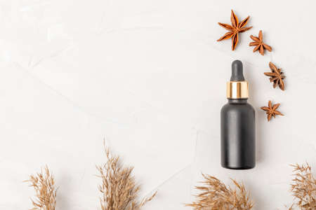Black cosmetic bottle with a dropper near anise and dried flowers on a white background. Flat layの写真素材