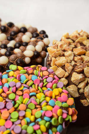 Three marshmallows in chocolate with multi-colored confetti, nuts and waffle topping closeupの写真素材