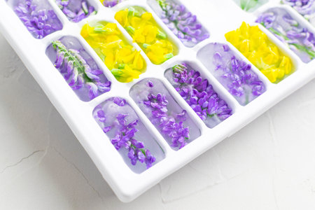 Ice cubes with yellow and violet flowers in a tray close-up. Bright hues