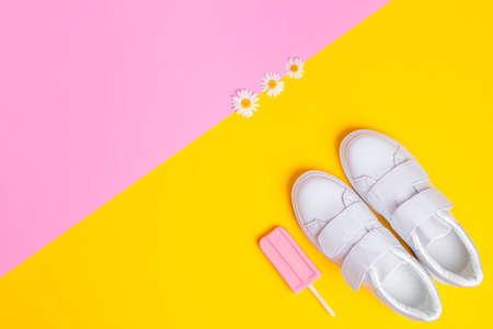 White sneakers and pink ice cream on a yellow pink background in the corner of the frame. Three daisies lie nearby. View from above. Bright summertime conceptの写真素材