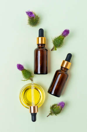 Flat lay of cosmetic glass brown bottles with dropper, burdock flowers and oil on mint backgroundの写真素材