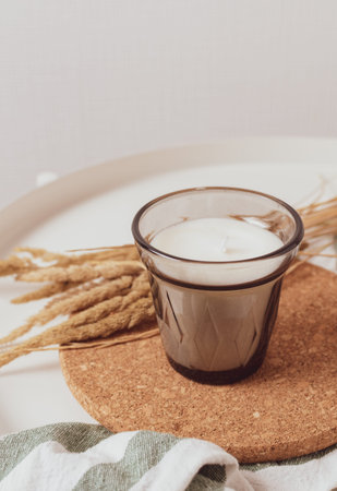 A candle in a glass beaker on a cotton napkin on a white table, next to it is a bouquet of dried...