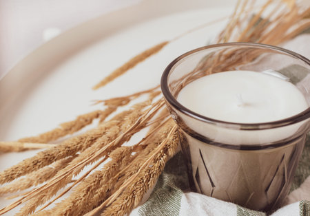 A candle in a glass beaker on a cotton napkin on a white table, next to it is a bouquet of dried...