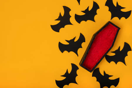 Halloween background in yellow color with silhouettes of bats and a small wooden black and red coffin. Flat lay, copy spaceの写真素材