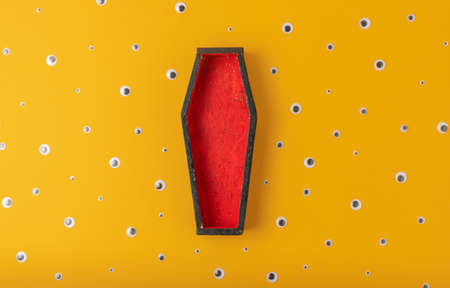Halloween yellow background with an open red-black coffin in the center, around a scattering of plastic eyes of different sizes. A place for your productの写真素材