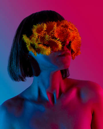 Portrait of a young woman in neon bright blue and pink colors. A blindfold of dandelion flowers is on the eyesの写真素材