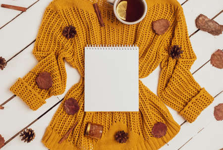 Cozy flat lay of notepad, cups of lemon tea, yellow sweater, leaves, cinnamon sticks and pine cones on white wooden background. Autumn composition with place for textの写真素材