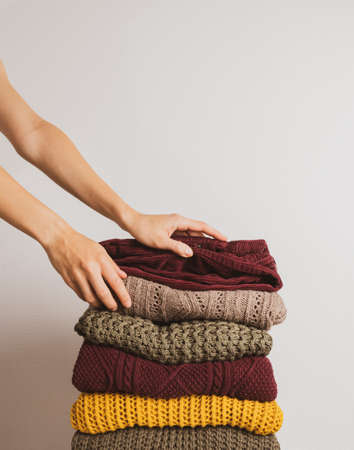 A woman takes a sweater from a stack of warm things on a white background. Faceless. Autumn color paletteの写真素材