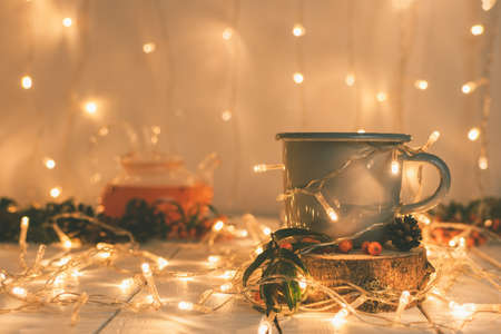 New Year's composition in warm muted colors from a cup of sea buckthorn tea on a wooden cup holder, a teapot and a festive garlandの写真素材