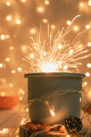 Christmas composition in warm muted colors from a cup of sea buckthorn tea on a wooden cup holder in the foreground, a sparkler, a teapot and a festive garlandの写真素材