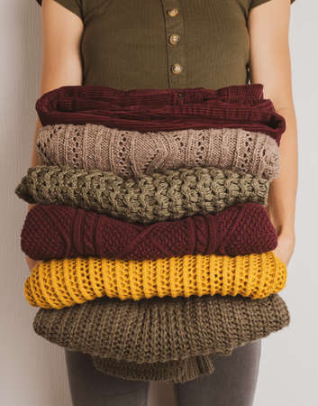 A young woman holds a stack of warm clothes in autumn colors. Sweaters in yellow, dark green, brownの写真素材