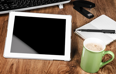 Tablet with an empty screen laid on a table close to a pen and green cupの写真素材