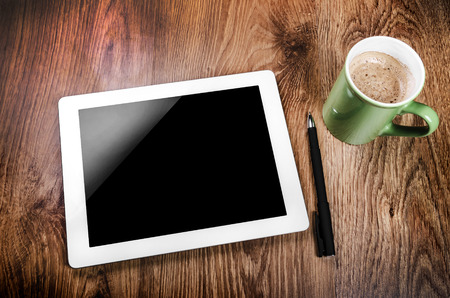 Tablet with an empty screen laid on a table close to a pen and green cup の写真素材