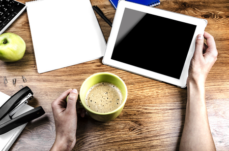 Tablet with an empty screen in hands close to a pen and  cupの写真素材