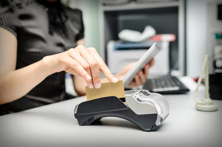 Female hand holding  bank terminal and tablet pc