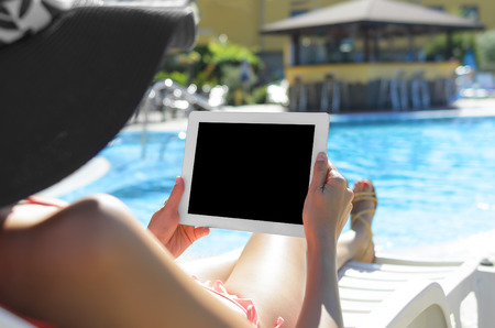 Woman with tablet pc sitting at swimming poolの写真素材