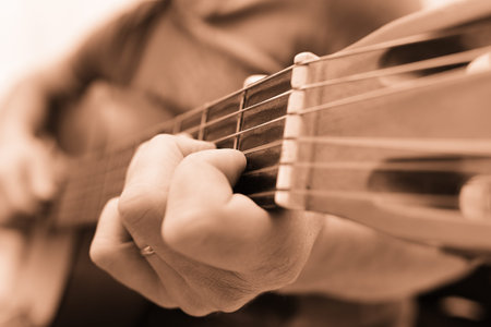 Man playing acoustic guitar at home, hand close-up.
