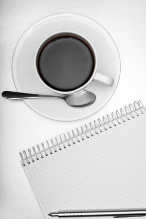 Blank notepad, a pen and a cup of coffee on a white tableの写真素材