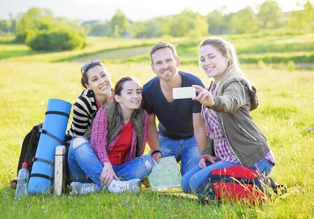 Group hikers on the grass with backpack taking selfie at sunset.の写真素材