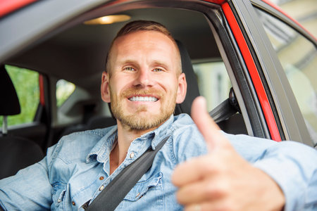 Man at the wheel of his new car, showing thumb up.