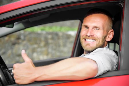 Man at the wheel of his new car, showing thumb up.