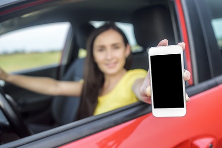 Woman sitting in a car and showing her smartphone out the window.の写真素材