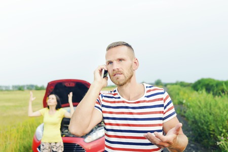 Damage to auto. Young man call for help on the phone. Young couple can not continue the way because of the broken car.の写真素材
