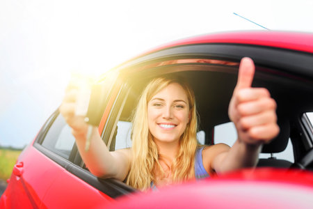 Happy woman in red car showing thumb up and key.