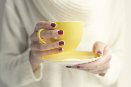 Cup with a hot drink in female hands close up. Soft style toned photo.の写真素材