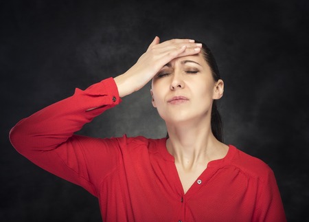Woman experiencing a headache. On a dark background.の写真素材