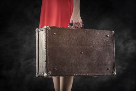 Old suitcase in hands on a dark background. Travel vintage concept.の写真素材