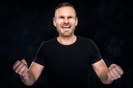 Man in black celebrate success on dark background.
