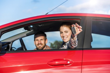 Attractive couple in the red car with the keys of the car at sunset.の写真素材
