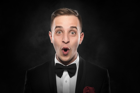 Portrait of surprised man in suit with bow-tie over dark background.の写真素材
