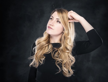 Thinking blond woman on a dark background. Free space for your text or image.の写真素材