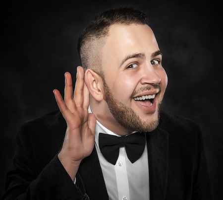 Man with big ear listening something on a dark background.の写真素材