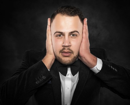 Man in suit covering his ears over dark background.の写真素材