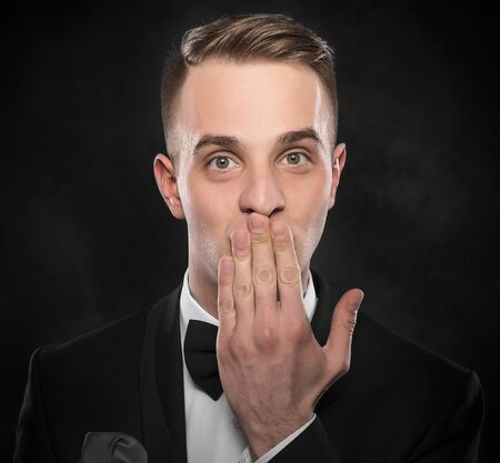 Scared man in suit hand covering mouth over dark background.の写真素材