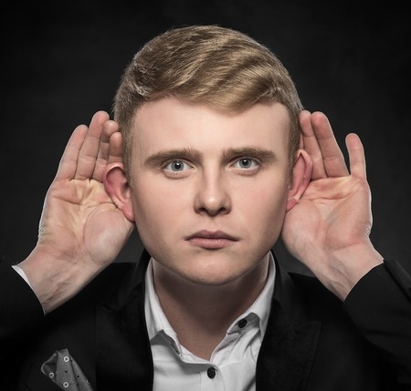 Man with big ear listening something on a dark background.の写真素材