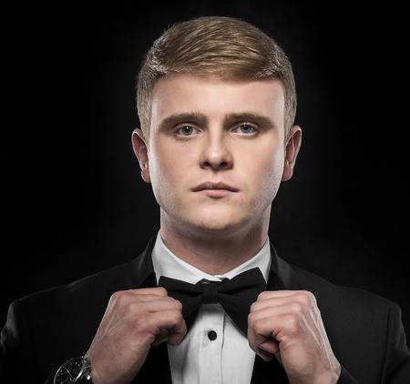 Young handsome man in suit with bow-tie on dark background.の写真素材
